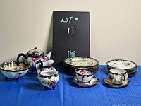 Full view of antique Nippon tea set with multiple porcelain items shown on a blue tablecloth, including plates, cups, teapot, and sugar and cream dishes.