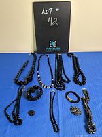 Jewelry lot items arranged on a blue surface including necklaces, bracelets, and brooches with a black sign labeled Lot #42.