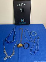 Photo of all blue costume jewelry on a blue cloth including several necklaces and bracelets.