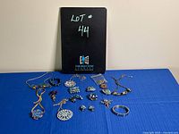 Full lot of blue-based costume jewelry displayed on blue textured surface, includes various necklaces, brooches, bracelets, and earrings with blue and green tones.