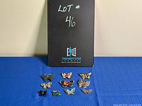 Photo showing 10 butterfly brooches arranged on a blue cloth with a black sign indicating lot number 46.