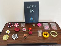 Complete overview of the lot arranged on a wood table, showing primarily flower brooches, some bracelets, and small packaged clip earrings.
