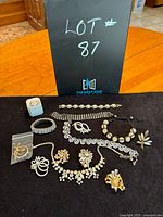 Photo of all costume jewelry items in the lot arranged on a black cloth with a black board labeled Lot 87 in the background