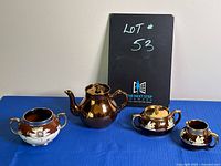 Four ceramic/porcelain items: Gibson teapot, Gibson creamer, Burslem sugar bowl with two handles, and Burslem covered sugar bowl or teapot arranged on table.