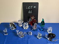 Photo showing entire lot with all glass animal figurines arranged on a blue cloth background with a black sign reading 'LOT 66'.