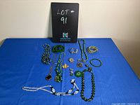 Overview of all green costume jewelry items including necklaces, bracelets, pins, and earrings, laid out on blue fabric.