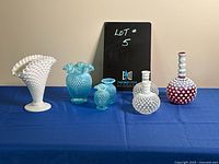 Full set of six Hobnail glass pieces on blue cloth with black sign behind them, showing their shapes and colors.