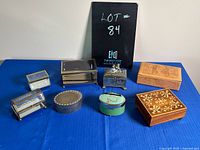 Photo showing nine assorted vintage jewelry boxes arranged on blue cloth, featuring various shapes, materials, and designs.