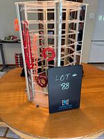 Clear plastic octagonal spinning jewelry display tower on wood table with multiple rods and hanging red and orange costume jewelry pieces such as beaded necklaces and bracelets.