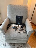 Front view of grey upholstered lift chair showing rolled arms, cushioned back, seat and included remote control and paperwork on seat