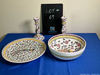 Overview photo showing the serving plate, bowl, and two taper candle holders side by side on a blue cloth surface with a black lot sign behind them.
