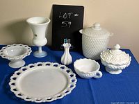 Full view of all milk glass and hobnail glass items on blue cloth, showing plate, pedestal bowl, covered containers, hobnail bowl, and opaline vase.