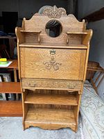 Front view of oak secretary desk with closed drop-down table, showing carved drawer and decorative top with circular mirror