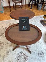 Photo of two vintage oval walnut occasional tables, one with a solid wooden top and the other with an oval glass inset top on wooden frame. Both rest on tripod style legs.