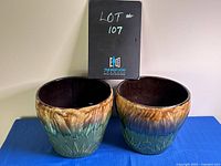 Two green and brown ceramic planter pots side by side showing front embossed detail and gradient glazed finish.