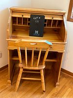 Front view of vintage pine roll top desk with included matching wooden chair, showing desk compartments and chair front.