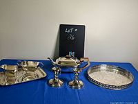 Full view of silver plate assortment laid out on blue cloth including tray, candlesticks, tea pot, and round tray.