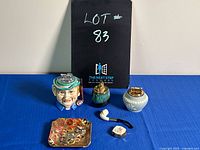 Overview of vintage ceramic lighters and ashtray atop a blue cloth background with black lot number card