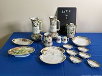 Full assortment of Nippon porcelain items displayed on blue cloth, showing two tall jugs with floral and gold decoration, smaller dishes, salt and pepper shakers, and other serving pieces.