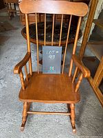 Front view of vintage wooden rocking chair with spindle back, curved top rail, and armrests showing light wear.