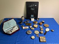 Wide view of all items arranged on blue cloth, including vintage children’s cutlery set in original case, assorted pill boxes and compacts.