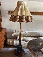 Side view of vintage wooden floor lamp showing full height, wooden base, stem, and pleated cream fabric lampshade with floral decorative band.