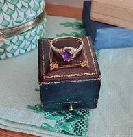 Ring displayed on small decorative box, front view highlighting amethyst
