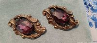 Front view of both brooches showing purple stones and ornate metalwork