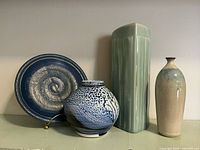 Four pieces of studio pottery: blue stoneware plate, blue-white globe vase, tall celadon triangular vase, slender gradient vase