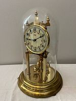 Full view of brass Kundo anniversary clock under glass dome