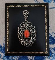 Pendant on top of presentation box showing ornate design and coral stone