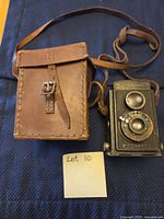 Kodak Brownie camera next to stitched leather case on blue cloth background