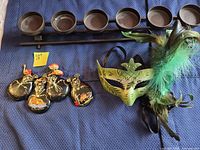 All lot items: five castanet pairs, mask, candle holder laid on blue surface