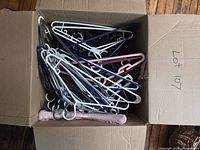 Open cardboard box showing large quantity of assorted plastic and wire clothes hangers