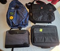 All four bags laid out on table: backpack, SwissGear messenger, grey sleeve, black briefcase