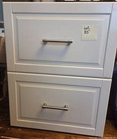 Front view of white IKEA two-drawer cabinet with hardware installed, lot sticker visible