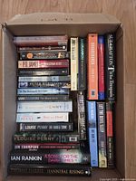 Box containing two stacks of murder mystery novels with readable spines