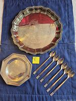 Two silver-plate platters and six stainless steel spoons displayed on blue cloth