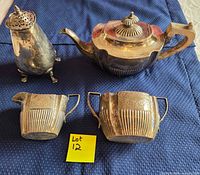 Top view of four silver plated pieces: teapot, sugar bowl, creamer, salt shaker on blue cloth