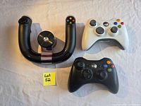 All three controllers arranged on a table: white gamepad upper right, black gamepad lower right, black wireless speed wheel left