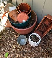 General overview of assorted plastic plant pots and saucers in mixed sizes and colors including terracotta and green placed on ground outside near wall.