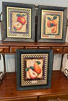 Set of three wood framed fruit art prints showing apple, apricot, and pear images with checkered borders.