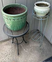 Two ceramic garden pots on metal pot holders; larger green pot and smaller cream-colored pot on stands.