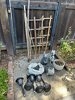 Photo showing garden statues, planters, solar lights, wooden stakes and trellises arranged on a concrete slab outside.