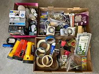 Wide view of the lot showing light bulbs, electrical timers, various types of tape, paint brushes, flashlights, gardening supplies, furniture pads, wall anchors, hooks, and a fix-it kit.