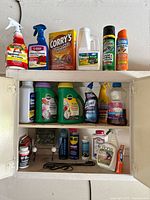 Photo showing multiple household and garden chemical and cleaning product bottles and cans on shelves inside a cabinet.