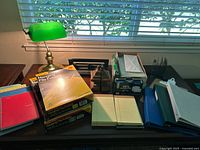 Photo of desk lamp with hanging file folders, note pads, hole punch and book ends on table near window with blinds.
