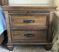 Front view of one nightstand showing two drawers with metal cup pulls on the lower drawers and a smaller top drawer with a round knob pull.