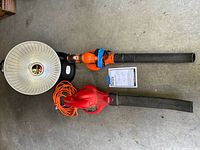 Presto HeatDish electric heater, BLACK+DECKER and Troy-Bilt electric leaf blowers placed on concrete floor with manual.