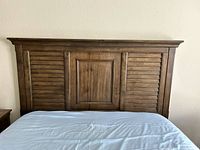 Front view of queen size wooden headboard with central panel and shutter style side panels in medium brown finish.